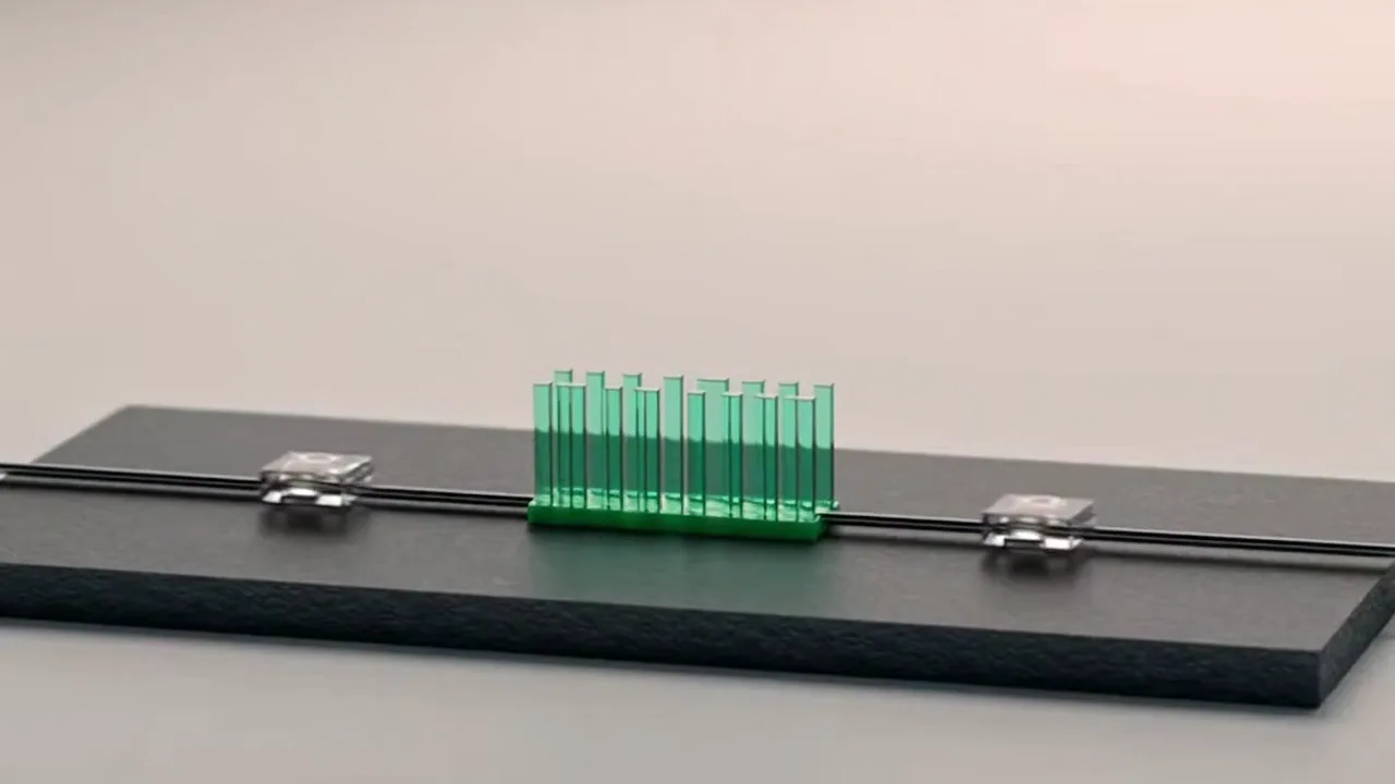 A small clear glass chip resting on a dark cable before an upright emerald glass approval gate on a charcoal slate slab, with a second chip already through on the far side.
